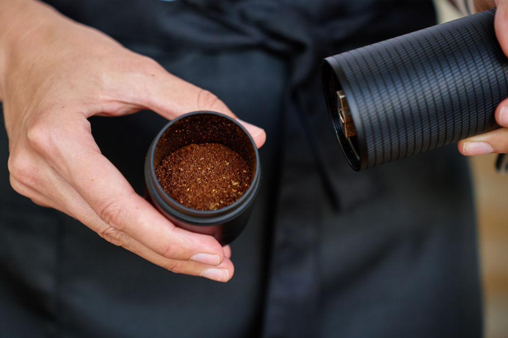 Hands holding the catch cup of a hand grinder, filled with freshly ground coffee.
